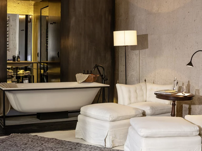Luxurious bathroom with freestanding BetteLux Shape bath, surrounded by cosy armchairs and dimmed, warm light; a mixture of spa and living room atmosphere for maximum relaxation.