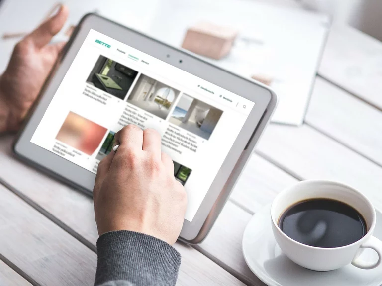 Person uses a tablet to scroll through the Bette website while a cup of coffee stands next to it - symbolising access to online information and press releases.
