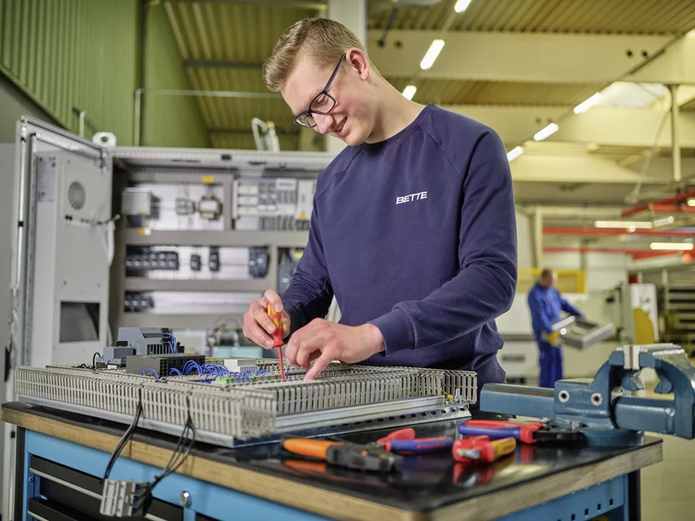Ein Auszubildender zum Elektroniker bei Bette arbeitet an einer Schaltanlage, mit Schraubendreher und Präzisionstechnik