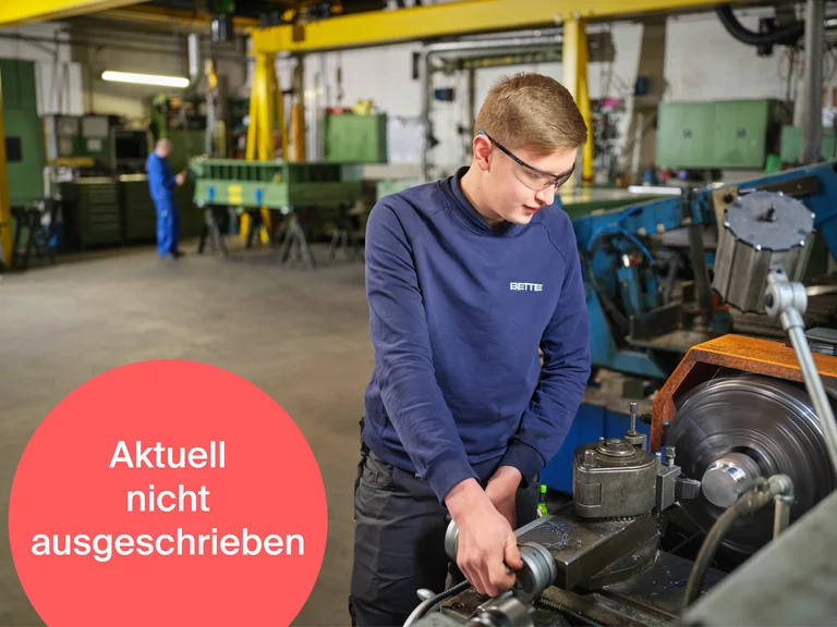 Ein Auszubildender zum Industriemechaniker bei Bette arbeitet an einer Drehmaschine in der Produktion. Ein roter Hinweis mit der Aufschrift 'Aktuell nicht ausgeschrieben' signalisiert, dass die Stelle derzeit nicht verfügbar ist.