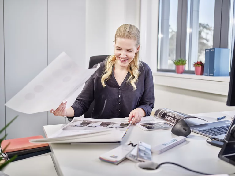 Auszubildende zur Kauffrau für Marketingkommunikation bei Bette beim Durchsehen von Marketingunterlagen an ihrem Schreibtisch