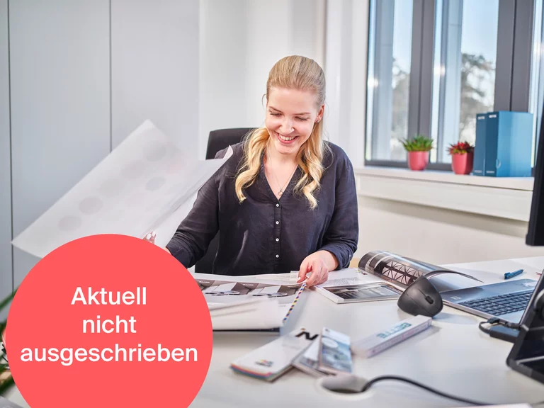 Auszubildende zur Kauffrau für Marketingkommunikation bei Bette beim Durchsehen von Marketingunterlagen an ihrem Schreibtisch. Ein roter Hinweis mit der Aufschrift 'Aktuell nicht ausgeschrieben' signalisiert, dass die Stelle derzeit nicht verfügbar ist.