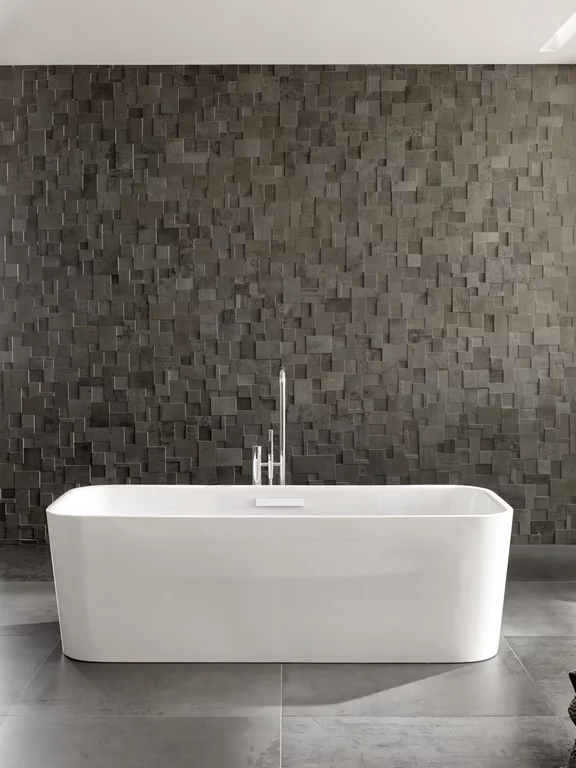 BetteArt: отдельно стоящая прямоугольная ванна перед темной каменной стеной на темно-серой плитке.