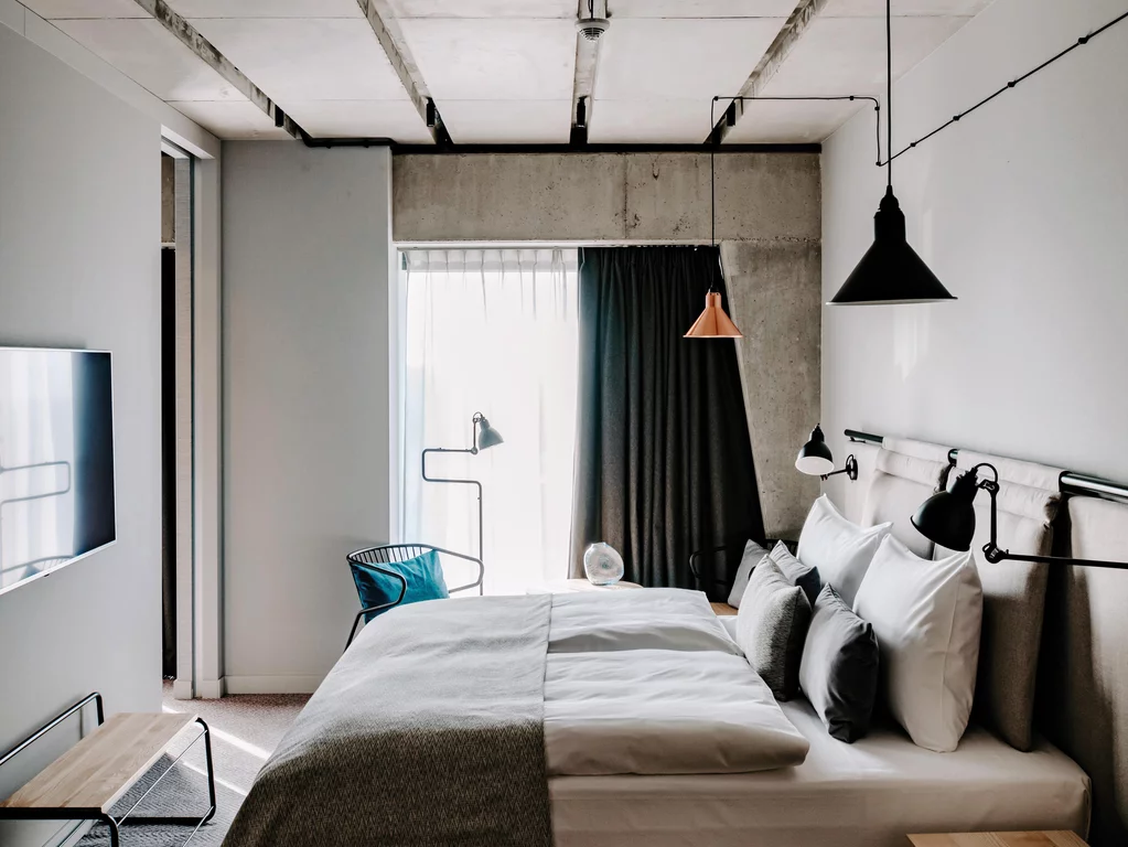 Bedroom at the Vienna House Mokotow, Warsaw. The bedrooms at Vienna House Mokotow, Warsaw, combine materials such as concrete, wood and wool with warm tones.