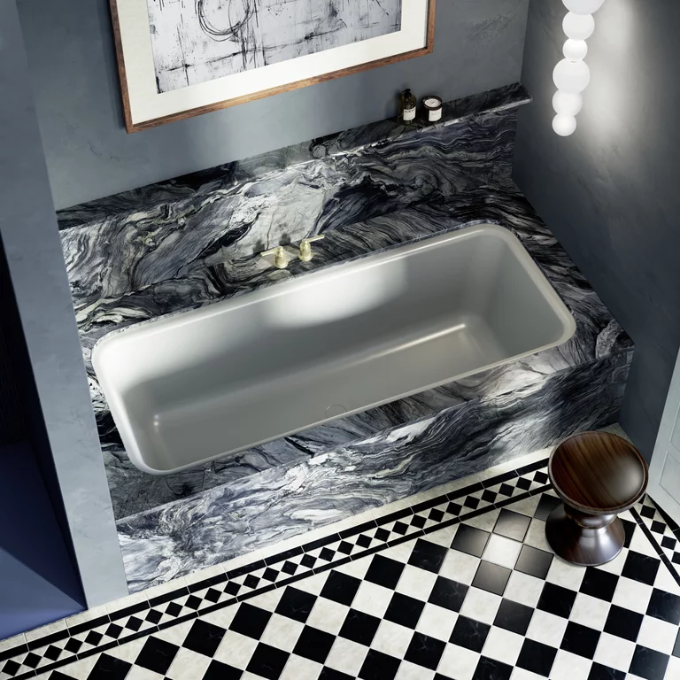 Luxe badkuip in grijs marmer met gouden kraan, omgeven door donkere muren en zwart-wit geblokte tegelvloer.