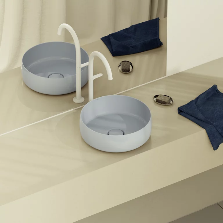 Modernes Bad mit rundem, hellblauem Aufsatzwaschbecken, weißer Armatur, Spiegel und beiger Konsole mit dunklem Handtuch.