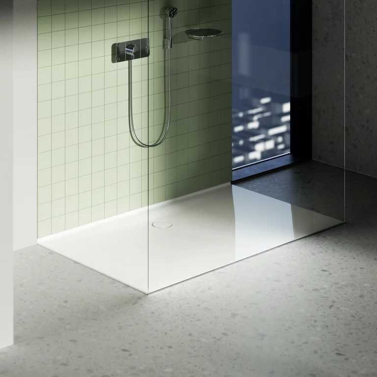 Moderne Dusche mit bodengleicher weißer Fläche, Glaswand, grüner Fliesenwand und Blick auf die Stadt durch großes Fenster.