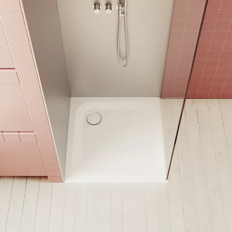 Detailansicht einer weißen Duschwanne mit Glasabtrennung, rosa Fliesen und hellen Holzdielen in modernem Bad.