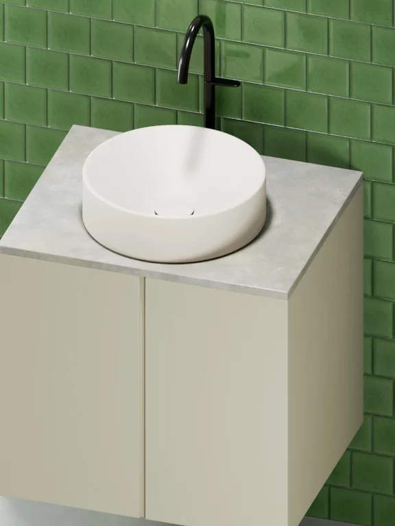 Vasque à poser BetteSuno de couleur flax avec une vasque ronde blanche sur un plan de travail gris, intégrée dans un meuble bas clair, devant un mur de carreaux verts brillants.