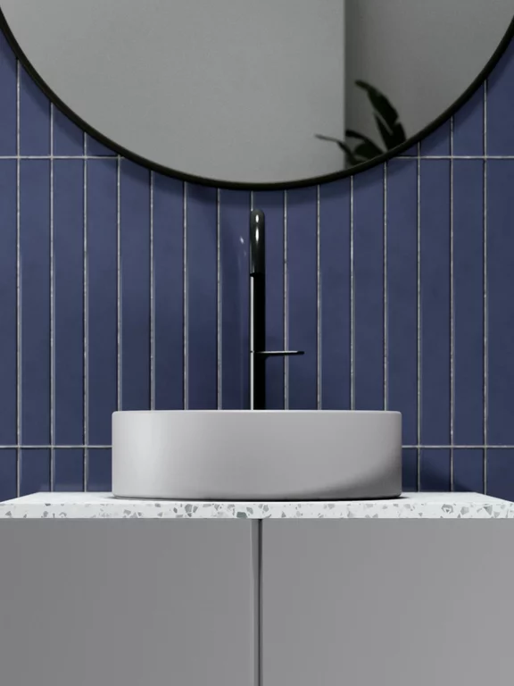 Vasque à poser BetteSuno de couleur silver avec vasque ronde et robinetterie noire, placée sur un plan de travail en terrazzo clair, devant un mur de carreaux bleus verticaux, complété par un grand miroir rond.