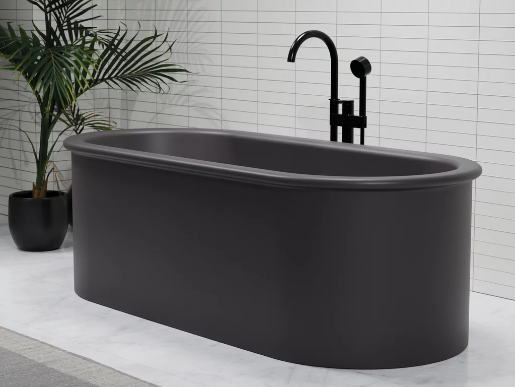 Baignoire autoportante BetteSuno de couleur graphite avec des bords doux et arrondis, équipée d'une robinetterie noire, devant un mur avec des carreaux blancs.