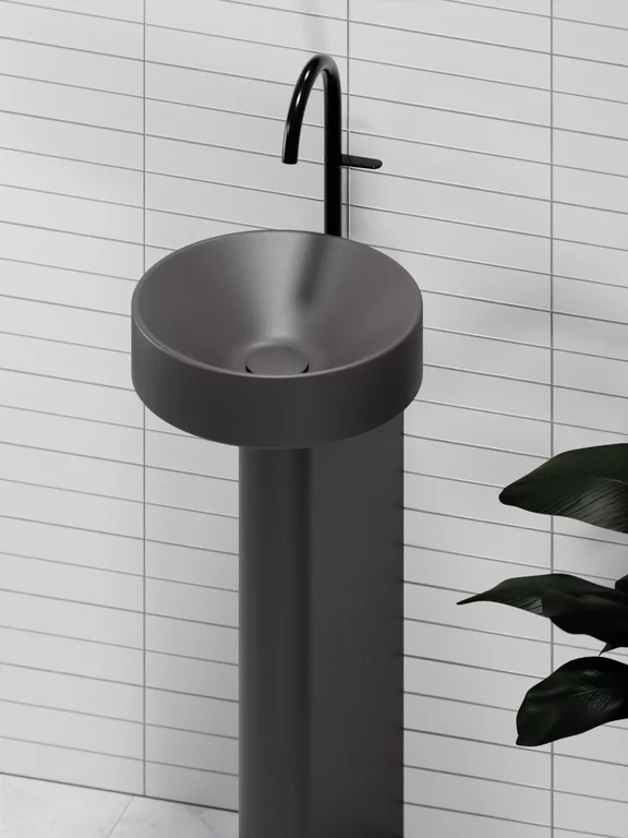 Vasque BetteSuno Pedestal de couleur graphite avec vasque ronde, socle indépendant et robinetterie noire, placée devant un mur de faïence claire.