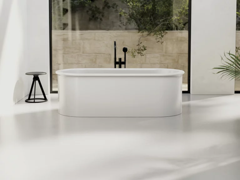 BetteSuno: Freistehende, ovale Badewanne in minimalistischem Design mit schwarzer Armatur, platziert vor großen Fenstern mit Blick auf eine Steinmauer und grüne Pflanzen.