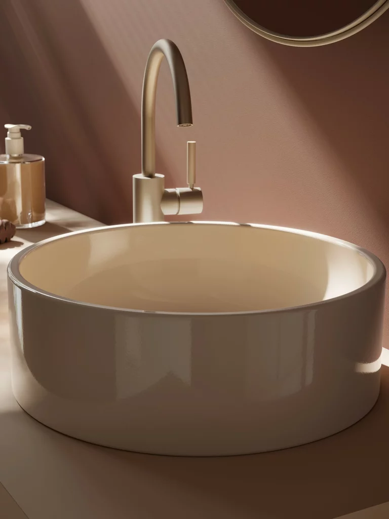 Close-up van een moderne, ronde BetteBalance wastafel in bahama beige en een elegante, goudkleurige kraan. Subtiele licht- en schaduweffecten benadrukken het hoogwaardige oppervlak en het minimalistische ontwerp.