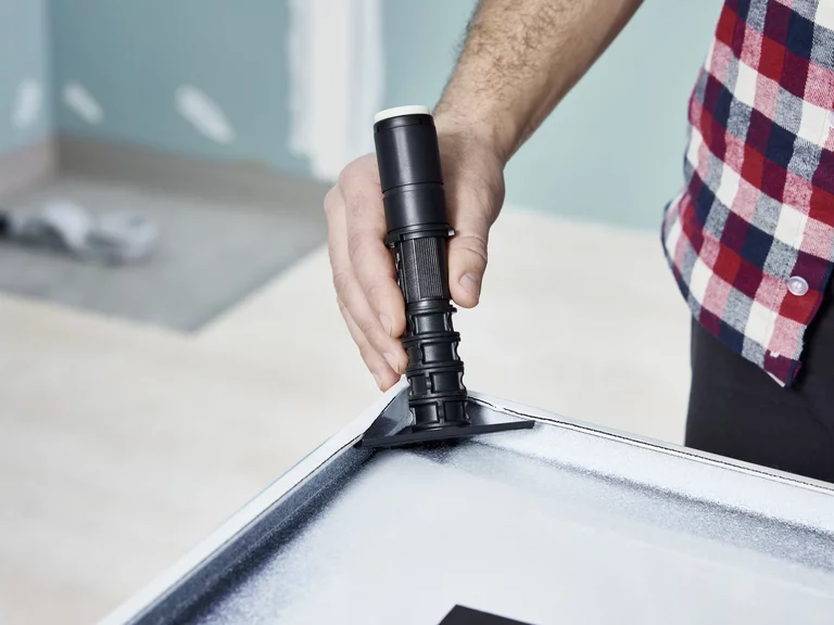 Человек устанавливает регулируемую по высоте ножку на душевой поддон при подготовке к монтажу.