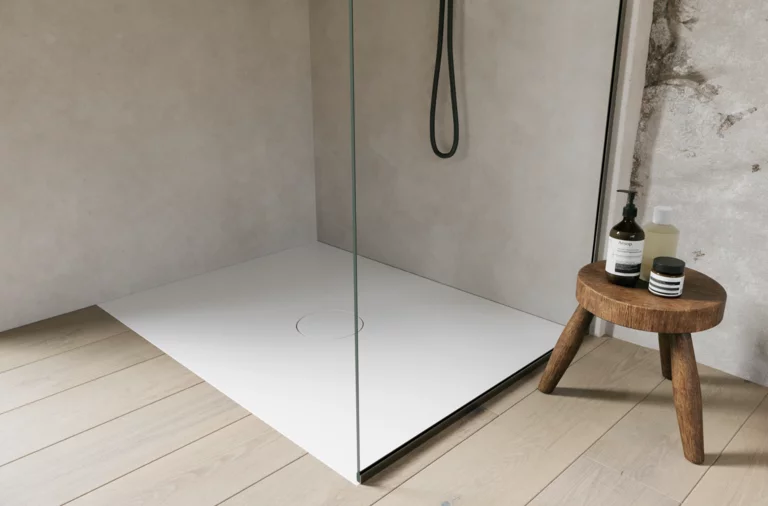 Witte inloopdouchebak met glazen wand en zwarte douche, naast een klein houten krukje met verzorgingsproducten.