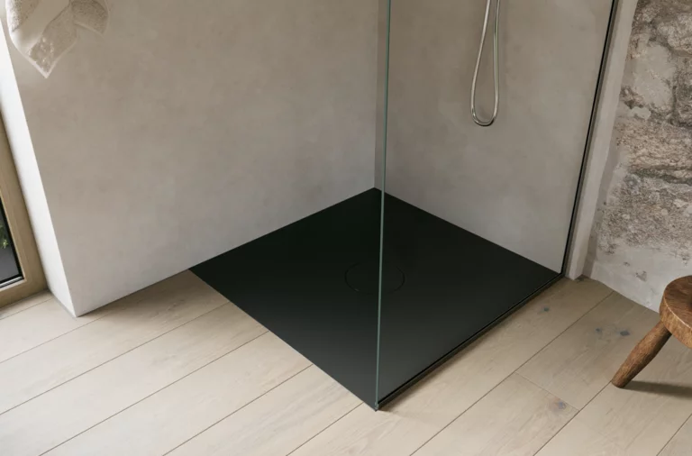 Zwarte inloopdouchebak met glazen wand en zilverkleurige douche in een lichte, minimalistische badkamer.