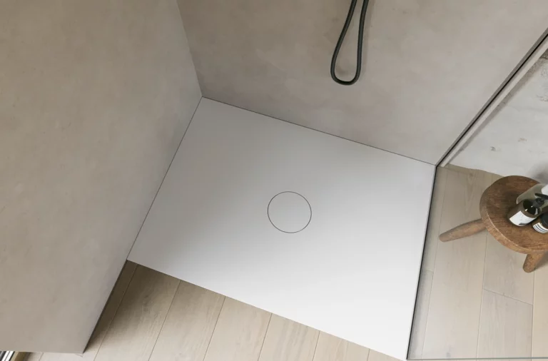 Witte inloopdouchebak met ronde afvoer, glazen wand en zwarte douche, schuin van boven gezien.