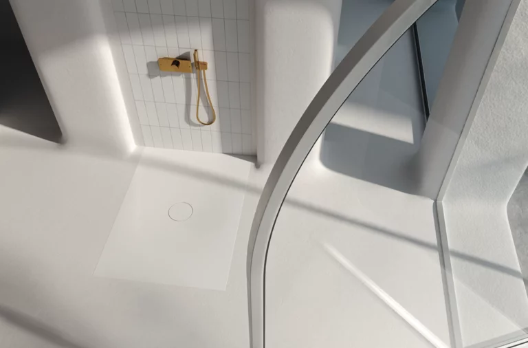 Receveur de douche rectangulaire en acier émaillé à entrée plate, de plain-pied, dans une douche moderne et lumineuse avec robinetterie dorée.