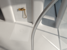 Rectangular steel enamel shower tray with low entry, flush with floor, in bright modern shower with gold fittings.