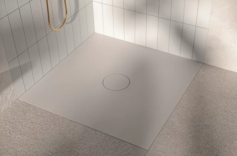 Receveur de douche carré en acier émaillé, posé à plat, avec bonde centrale, entouré de carreaux clairs et de sol mat.