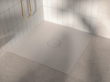 Receveur de douche carré en acier émaillé, posé à plat, avec bonde centrale, entouré de carreaux clairs et de sol mat.