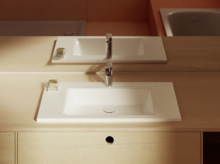 Прямоугольная белая раковина на светлой деревянной столешнице с зеркалом, мыльницей и современным смесителем.