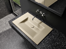 Прямоугольная стальная эмалированная раковина с четкими краями на тёмной столешнице, настенный смеситель сверху.