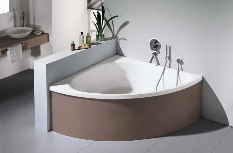 Baignoire en acier émaillé angulaire avec façade arrondie, robinetterie indépendante, lavabo sur plan en bois en arrière-plan.