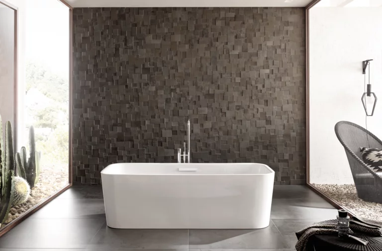 Отдельностоящая прямоугольная ванна из стальной эмали перед фактурной тёмной стеной в современной ванной.