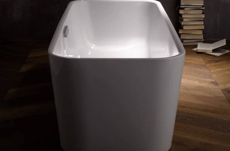 Отдельностоящая ванна из стальной эмали прямоугольной формы на деревянном полу, на заднем плане стопки книг.