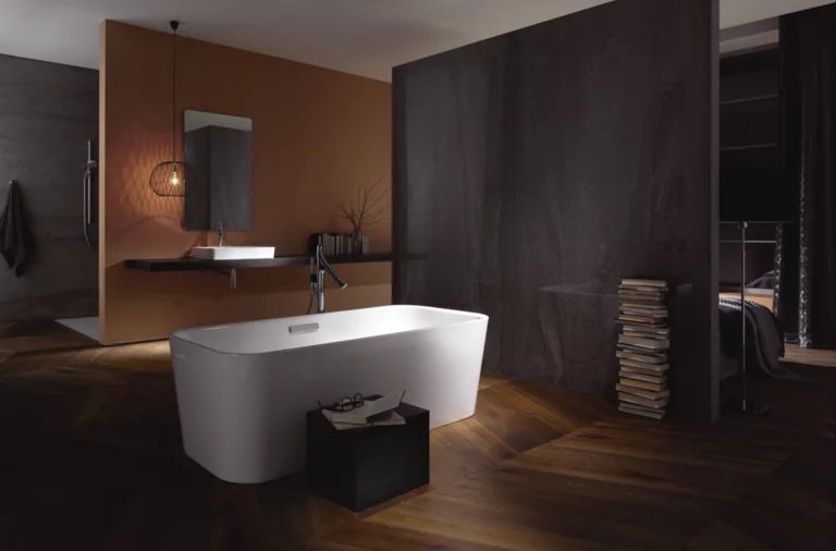 Freistehende, rechteckige Badewanne aus Stahl-Email, dahinter Waschbecken auf Einbauplatte, modernes Badezimmer mit Holzfußboden.
