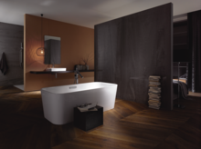 Freistehende, rechteckige Badewanne aus Stahl-Email, dahinter Waschbecken auf Einbauplatte, modernes Badezimmer mit Holzfußboden.