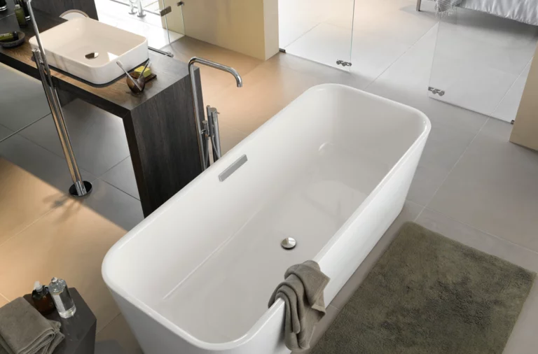 Freistehende, rechteckige Badewanne aus Stahl-Email, daneben eckiges Waschbecken auf dunkler Einbauplatte, modernes Bad.