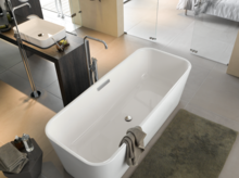 Freistehende, rechteckige Badewanne aus Stahl-Email, daneben eckiges Waschbecken auf dunkler Einbauplatte, modernes Bad.