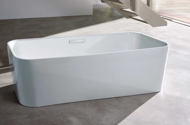 Freistehende Badewanne aus Stahl-Email, rechteckige Form, abgerundete Ecken, auf grauem Boden in modernem Raum.