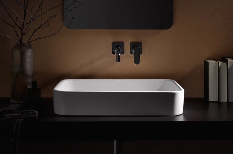 Lavabo rectangulaire en acier émaillé sur plan de travail sombre, robinetterie murale, environnement minimaliste.