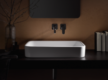 Lavabo rectangulaire en acier émaillé sur plan de travail sombre, robinetterie murale, environnement minimaliste.