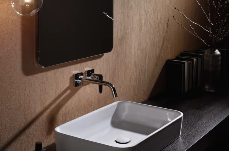 Rechteckiges Stahl-Email-Waschbecken auf dunkler Einbauplatte, Wandarmatur darüber, modernes Badezimmer-Design.
