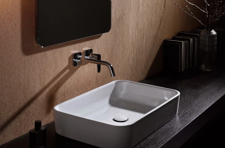 Lavabo rectangulaire en acier émaillé sur plan de travail foncé, robinet mural au-dessus, design de salle de bain moderne.