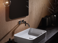 Rechteckiges Stahl-Email-Waschbecken auf dunkler Einbauplatte, Wandarmatur darüber, modernes Badezimmer-Design.