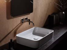 Lavabo rectangulaire en acier émaillé sur plan de travail foncé, robinet mural au-dessus, design de salle de bain moderne.