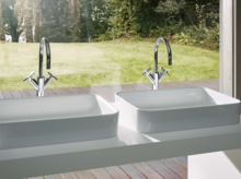 Deux lavabos rectangulaires en acier émaillé sur plan blanc avec robinetterie chromée, devant fenêtre.