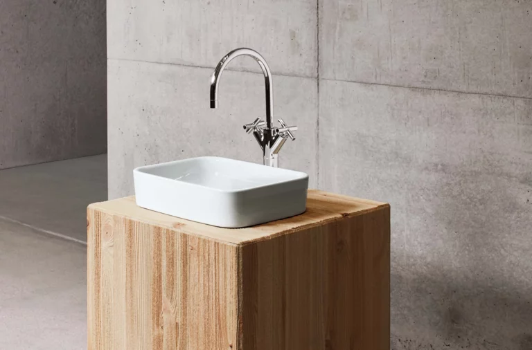 Rechteckiges Waschbecken aus Stahl-Email auf Einbauplatte, moderner Wasserhahn, minimalistisches Design vor Betonwand.