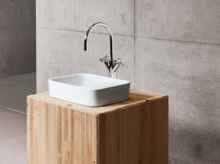 Rechteckiges Waschbecken aus Stahl-Email auf Einbauplatte, moderner Wasserhahn, minimalistisches Design vor Betonwand.