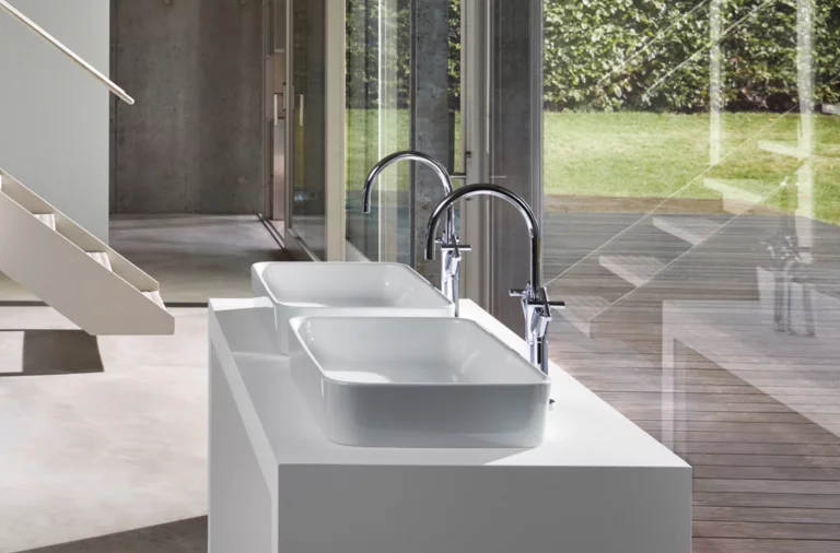 Deux lavabos rectangulaires en acier émaillé sur plan blanc avec robinetterie moderne, grandes fenêtres en arrière-plan.