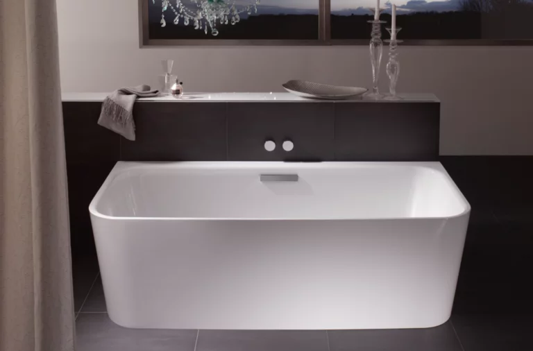 Freestanding rectangular steel-enamel bathtub in modern bathroom with chandelier and window in background.