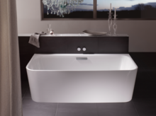 Freestanding rectangular steel-enamel bathtub in modern bathroom with chandelier and window in background.