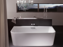 Freestanding rectangular steel-enamel bathtub in modern bathroom with chandelier and window in background.