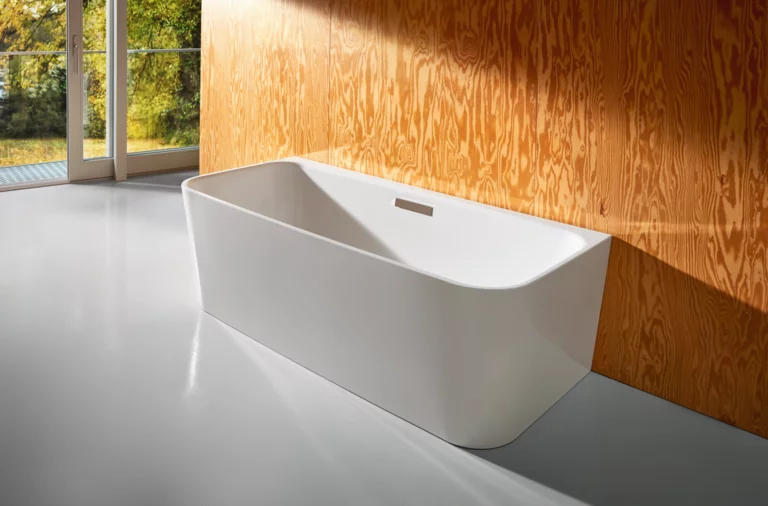 Freestanding rectangular steel enamel bathtub with rounded corners in front of a wood-effect wall.